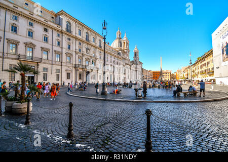 Tourists and locals enjoy a busy autumn morning inside the Piazza Navona in front of the Sant'Agnese in Agone Church in Rome, Italy. Stock Photo