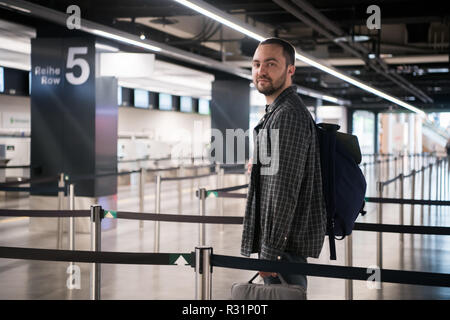 Young man with his luggage and backpack using smartphone while waiting for airline flight in the international airport terminal, travelling and online check in concepts Stock Photo