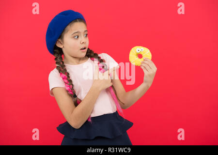 Sweets shop and bakery concept. Kids huge fans of baked donuts. Impossible to resist fresh made donut. Girl hold glazed cute donut in hand red background. Kid playful girl ready to eat donut. Stock Photo