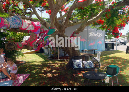 Yarn-bombed flowering Ponciana tree with outdoor chairs and tables, Two Sisters Cafe, Cooee Bay, Yeppoon, Queensland, Australia. No MR or PR Stock Photo
