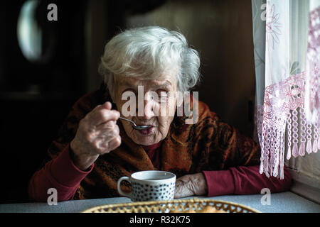 An elderly gray-haired pensioner woman drinking tea at home. Stock Photo