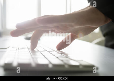 Businessman hand typing on black computer keypad lit by bright sun light coming from the windows in background. Stock Photo