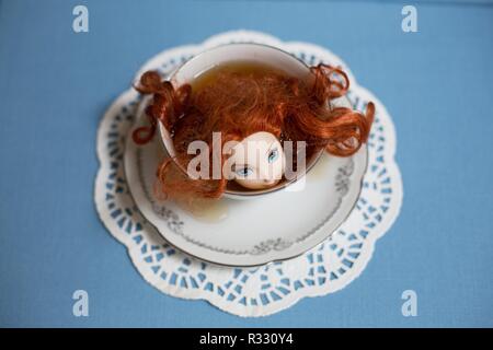 Surreal image of red-headed doll in a cup of tea. Stock Photo