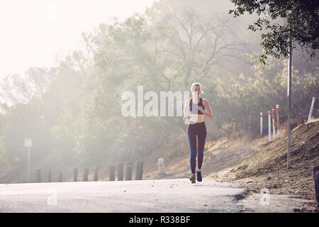 Beautiful Caucasian White Woman Runs Along the Road in the Morning Sunlight Stock Photo