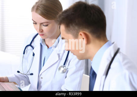 Doctors writing papers using clipboard. Physicians discussing medication program or studying at medical conference. Healthcare, insurance and medicine concept Stock Photo