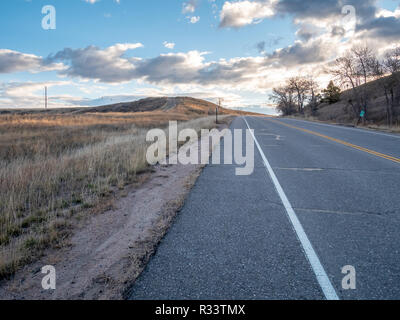 Low Angle View of Country Road Going Up Hill With Tall Dry Grass Fields on the Left Stock Photo