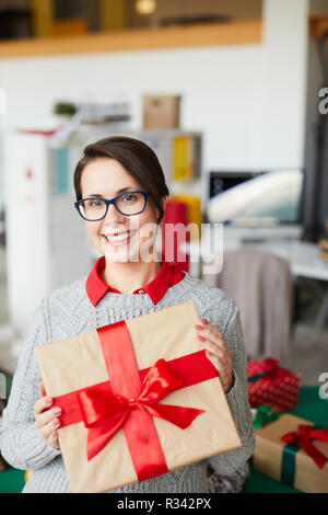 Young smiling female with packed box tied up with silk red ribbon showing it to you Stock Photo