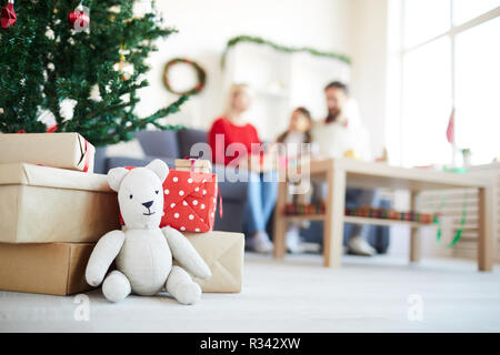 White teddybear and stack of packed gifts on the flooe by decorated firtree Stock Photo
