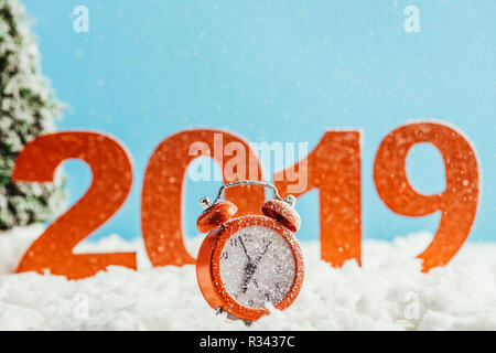 big red 2019 numbers with alarm clock standing on snow on blue background, new year concept Stock Photo