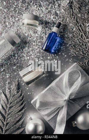 elevated view of composition with beauty cream, serum, micellar water and christmas decorations on silver Stock Photo