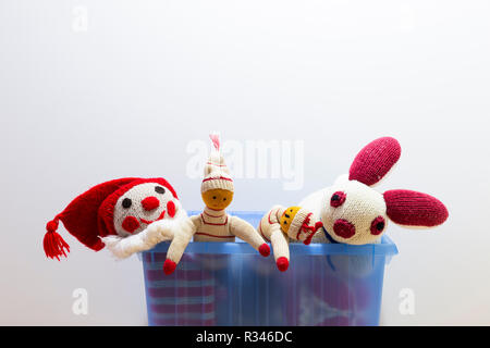 Cute and funny vintage children toys in a blue plastic box in front of a white wall. Assortment consists of a clown, a bunny and puppets. Stock Photo