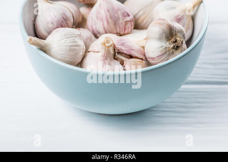 Garlic heads in blue ceramic bowl on white wooden kitchen table Stock Photo