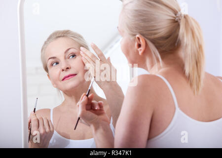 Forty years old woman looking at wrinkles in mirror. Plastic surgery and collagen injections. Makeup. Macro face. Selective focus on the face. Realistic images with their own imperfections. Stock Photo