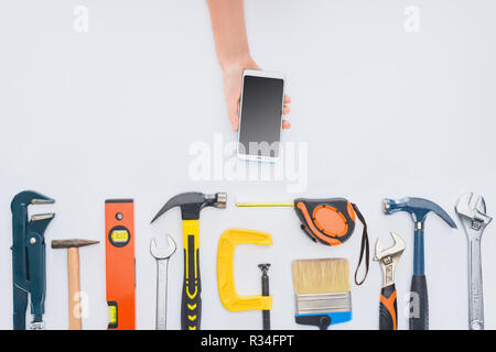 cropped shot of woman using smartphone with various tools lying on white Stock Photo