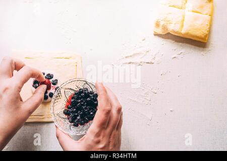 Cooking delicious sweets with jam and cinnamon and powder to tea.Top view. Womans hands are preparing a cake by laying berries on the dough. On a whit Stock Photo