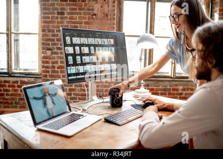 Young couple of photographers working with woman's portraits at the working place with two computers in the studio Stock Photo