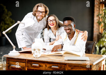 Portrait of a young multi ethnicity physicians or medical students in uniform sitting at the table in the office or classroom Stock Photo