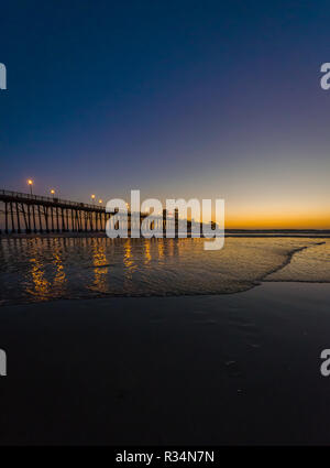 A pier reflecting on the surface of the ocean while the sun sets in Oceanside, California, USA Stock Photo