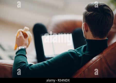 Young man with banana working on a laptop Stock Photo