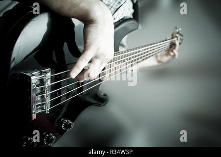 the musician plays on a black, shiny bass guitar Stock Photo