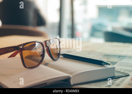 sunglasses, diary, pen and newspaper on the table in a cafe Stock Photo