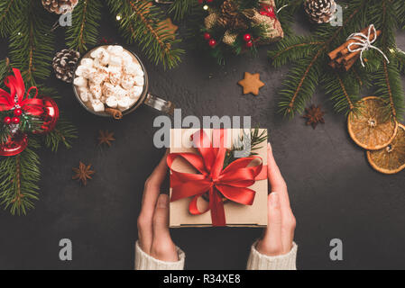 Christmas gift box in craft paper with red ribbon. Winter holidays New Year or Christmas background flat lay composition, person holding gift box Stock Photo