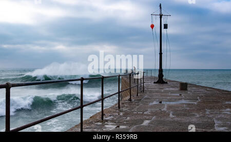 People at the end of the harbour wall in the distances seen from along the wall railings and into the huge waves being blown in the wind. Stock Photo