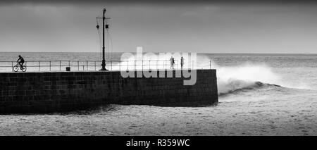 Black and white of rough seas hitting the harbour wall at Porthleven, Cornwall and soaking the onlookers in big waves. Stock Photo