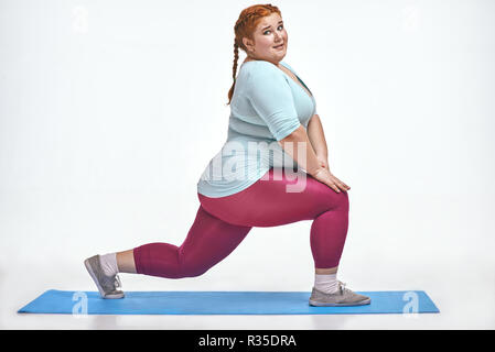 Amusing, red haired, chubby woman trains on the mat Stock Photo