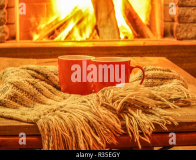 Orange mugs for tea or coffee; wool things against cozy fireplace background; winter vacations,horizontal. Stock Photo