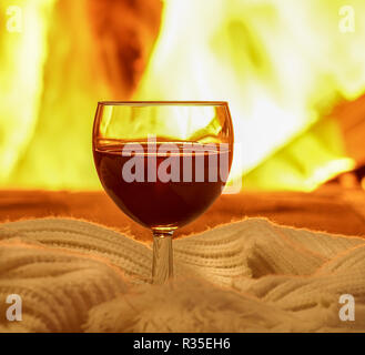 Glass of red wine; and wool; things against cozy fireplace background; winter vacation; horizontal; closeup; selective focus. Stock Photo