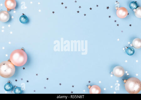 Christmas frame made of Christmas balls and silver confetti on blue background. Minimal New Year card, top view. Stock Photo