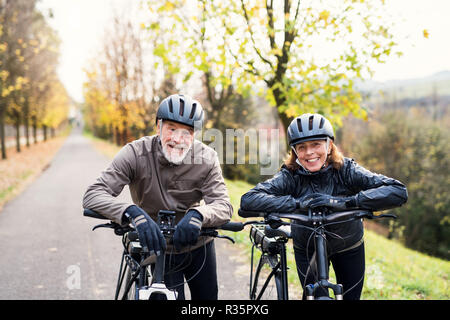 Active senior couple with electrobikes standing outdoors on a road in nature. Stock Photo