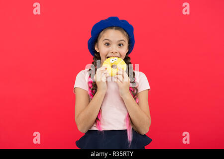 Kid smiling girl ready to eat donut. Sweets shop and bakery concept. Kids huge fans of baked donuts. Impossible to resist fresh made donut. Girl hold glazed cute donut in hand red background. Stock Photo