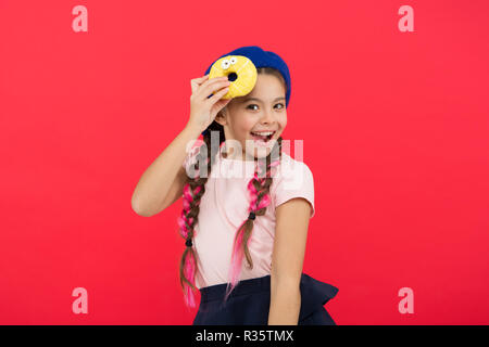 Impossible to resist fresh made donut. Girl hold glazed cute donut in hand red background. Kid playful girl ready to eat donut. Sweets shop and bakery concept. Kids huge fans of baked donuts. Stock Photo