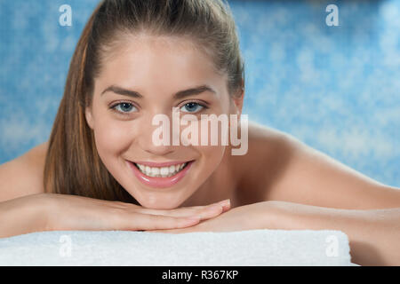 Closeup of attractive young woman lying on stomach on couch in spa salon, looking at camera and smiling. Woman posing during relaxing healthy procedure. Concept of massage and happiness. Stock Photo