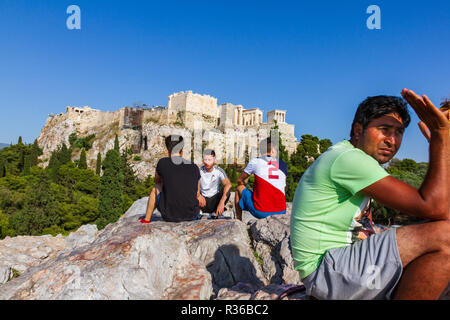 Athens, Greece - June 9, 2018: People seated on a rock and chatting against the Acropoilis ruins in Athens, Greece on a summer afternoon Stock Photo
