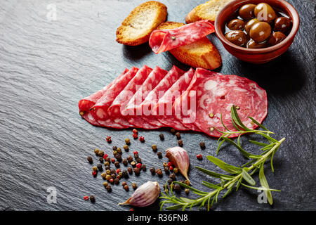 spanish dry-cured salchichon, Salami sausage slices on a black slate plate with toasts, olives and garlic, view from above, close-up Stock Photo