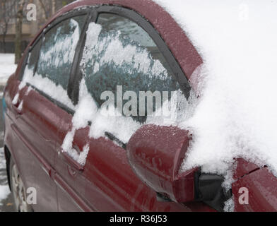 frozen iced car windows covered with snow. selective focus on rear mirror with blurred back of vehicle Stock Photo