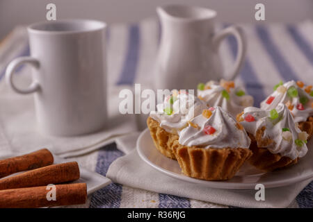 Delicious homemade cupcakes with cream, on a plate, a cup of tea and milk, cinnamon sticks, horizontal, soft focus. Stock Photo