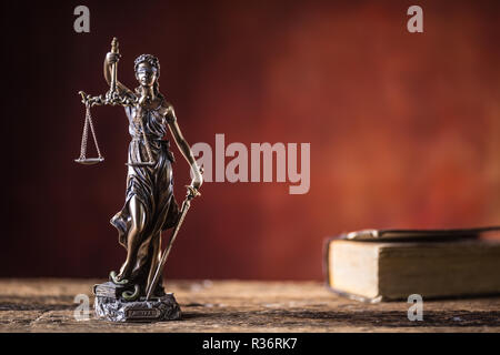 Lady Justicia holding sword and scale bronze figurine with book on wooden table. Stock Photo