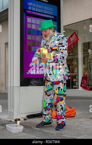 Bearded busker in a jazzy suit strums for donations in Liverpool City centre high street, as Black Friday discount sales get underway. UK Stock Photo