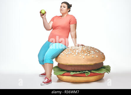 Brunette, funny, plump woman sits on a huge sandwich Stock Photo