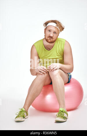 Red haired, bearded, plump man is sitting on a ball Stock Photo