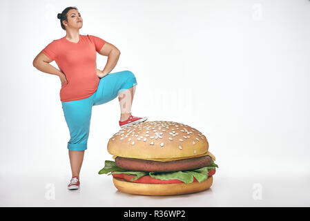 Brunette, funny, plump woman put her leg to a huge sandwich Stock Photo