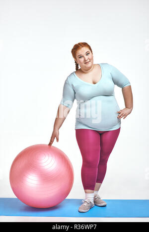 Funny picture of amusing, red haired, chubby woman which is holding a ball Stock Photo