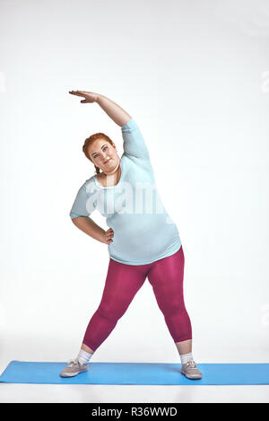 Amusing, red haired, chubby woman trains on the mat Stock Photo