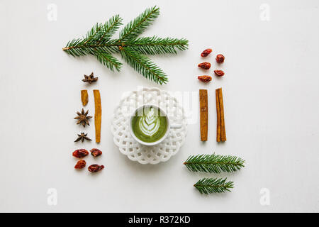 A cup of fragrant and tasty green matcha latte coffee on a white surface decorated in a Christmas style.