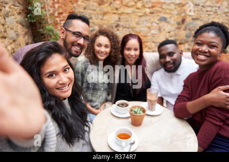 Diverse friends taking selfies in a trendy cafe courtyard Stock Photo