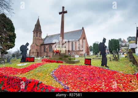 Knitted & crocheted red poppies on display together with standing soldier silhouettes, outside in UK churchyard, by war memorial. Armistice centenary. Stock Photo